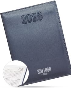 Agenda Diária 2025 de capa preta com detalhes dourados e páginas em branco, sobre uma mesa de madeira com caneta ao lado.