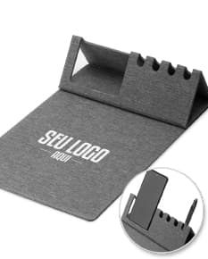 Mouse pad de couro marrom aberto em cima de uma mesa de escritório, ao redor estão um notebook preto, uma bolsa de couro, chaves, um cartão de crédito, uma carteira, um bloco de notas, um teclado preto e um mouse preto.
