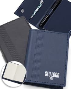 Bloco de anotações com porta caneta em um escritório vazio. O caderno está aberto em uma página em branco e ao lado há um videodisco. O design é moderno e conta com um espaço para guardar objetos, como canetas. O ambiente é limpo e organizado, com um ar de nostalgia.