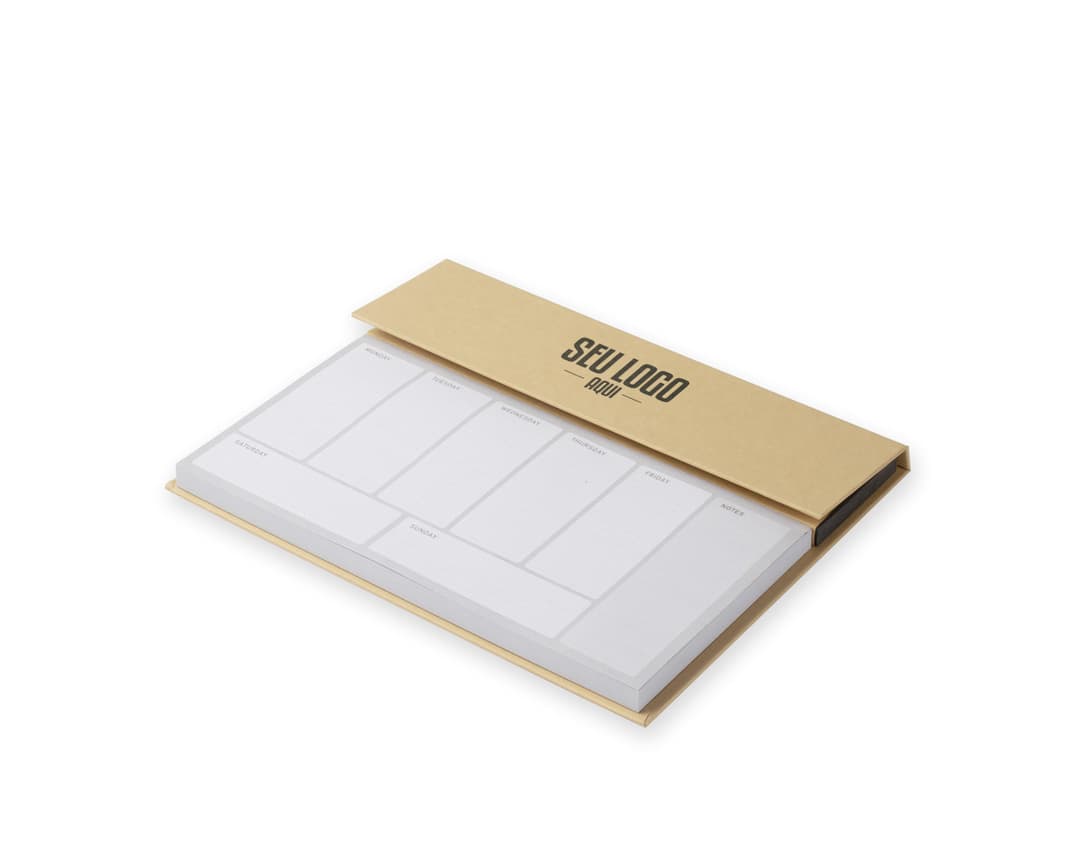 Bloco de anotações com planejamento aberto em uma mesa de escritório. No bloco, é possível ver páginas decoradas e datas planejadas. Além disso, há canetas e clips ao redor do bloco.