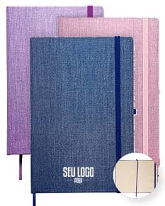 Caderneta A5 em papel texturizado antigo, com capa de tecido vintage em tom de marrom desgastado. O design é grunge e possui um padrão decorativo. O material é de fibra de algodão áspera, com uma superfície em canvas. Na capa, há um detalhe de costura em linha preta. O interior está em branco, com páginas vazias.